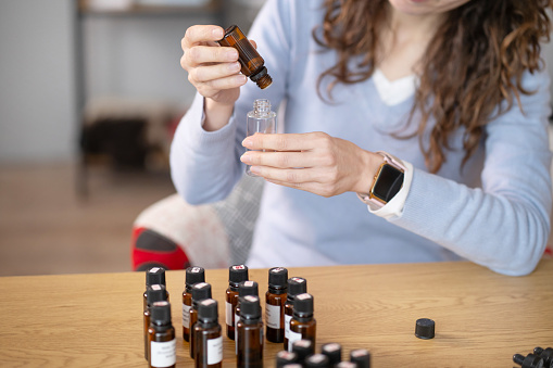 A woman is seated at a table with various bottles of essential oils, preparing a batch of bach flower remedy. She carefully selects and mixes the oils to create a personalized blend for therapeutic use.