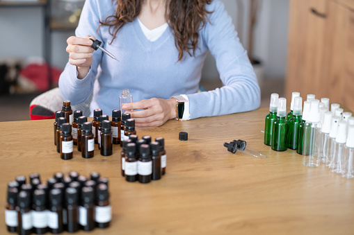 A woman is seated at a table, surrounded by numerous bottles. She appears to be carefully preparing Bach flower remedy using the various bottles and ingredients in front of her.