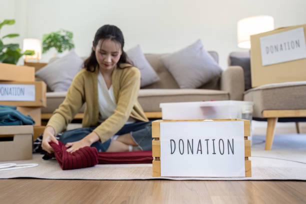 istock Asian young woman packing clothes at home, putting on stuff into donate box with second hand clothes 2050039862