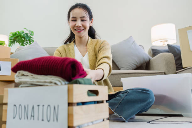 istock Asian young woman packing clothes at home, putting on stuff into donate box with second hand clothes 2050039892