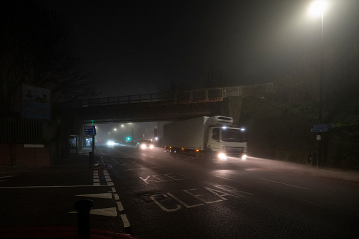 A truck passes under an overpass on a foggy night.