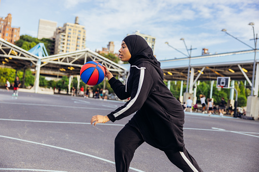 Muslim woman wearing a sport hijab playing basketball at the court.