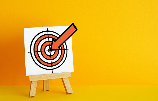 Archery target on a orange background. The concept of fulfilling the goal, striving to implement plans. Target with embedded arrow