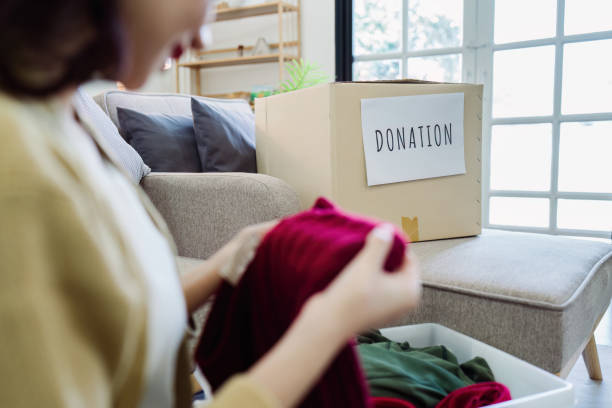 istock Asian young woman packing clothes at home, putting on stuff into donate box with second hand clothes 2050052859