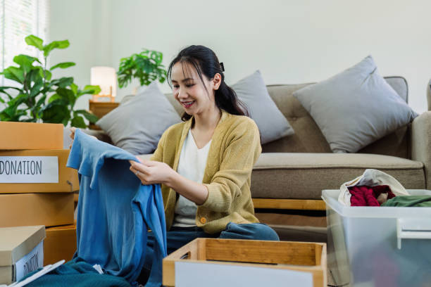 istock Asian young woman packing clothes at home, putting on stuff into donate box with second hand clothes 2050053402