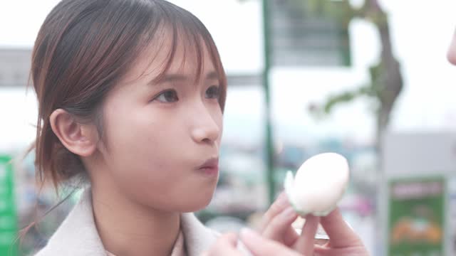 In Cheung Chang, Hong Kong, a young woman with long brown hair indulges in a white food item while clad in a white shirt and black jacket.