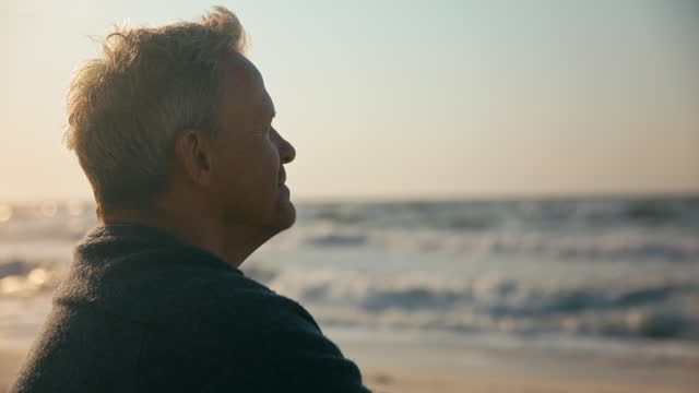 Peaceful Senior Man Relaxing Sitting On Beach Shoreline With Closed Eyes At Sunrise