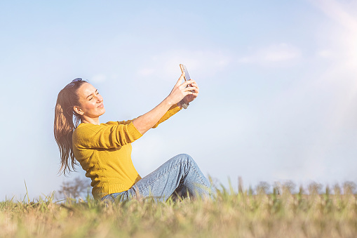 Woman is smiling in yellow take selfie on phone outdoor