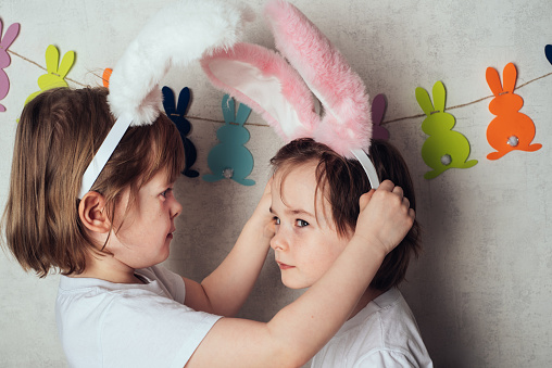 Portrait of girls, one puts a headband with bunny ears on the other. Preparation and celebration of Easter