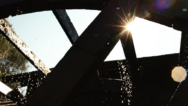 Low Angle View of Bright Sun Streaming through Watermill Spinning while Generating Hydroelectricity