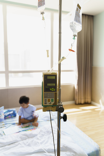 Selective focus on Intravenous IV drip medical machine in a hospital room with child patient in background.