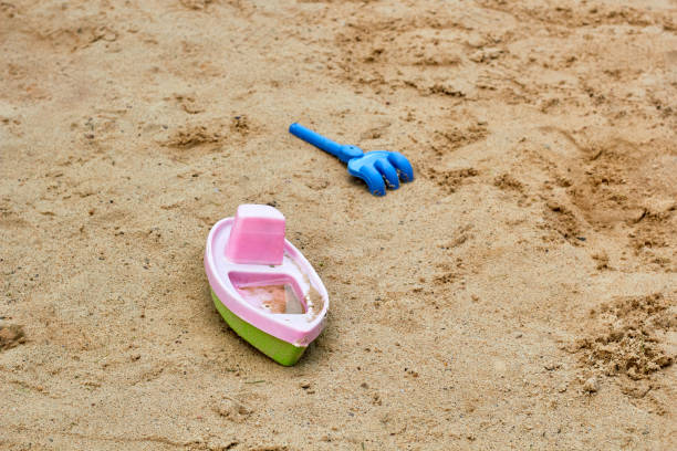 Plastic boat and blue rake on sand. Sand playground for children
