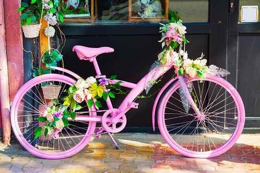 An urban pink bicycle decorated with flowers stands near the store.