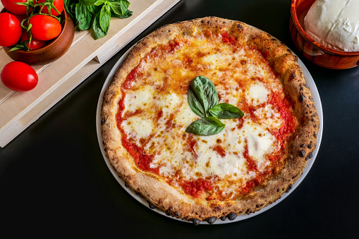 A delicious and tasty Pizza Margherita with fresh tomato sauce, Italian mozzarella, basil and extra virgin olive oil, rigorously cooked in a wood oven, according to the original Neapolitan tradition. In 2017 the art of Neapolitan Pizza was declared by UNESCO as an Intangible Cultural Heritage. Image in high definition quality.