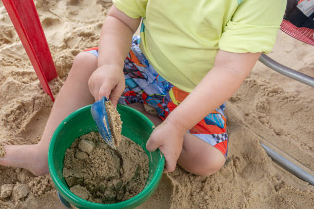 A young boy playing with sand in a green bowl while sitting on the beach
