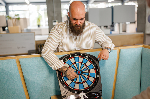 Young man removing darts out of dart board in modern office lobby