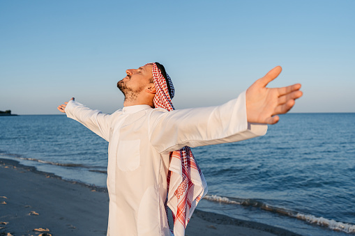 Handsome young man wearing keffiyeh and dishdasha and enjoying the view on the beach in Kuwait city in Kuwait.