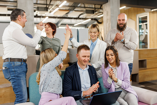 Happy coworkers giving high five while celebrating great teamwork result in modern office