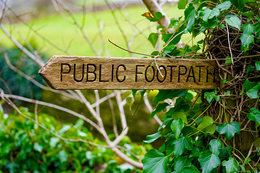 Wooden public footpath sign with green foliage