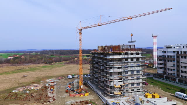 AERIAL Drone Shot of Construction Site with Unfinished Building and Crane Delivering Construction Material Under Sky