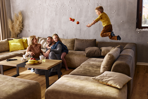 Carefree boy having fun while jumping on sofa during the time with his family at home. Copy space.