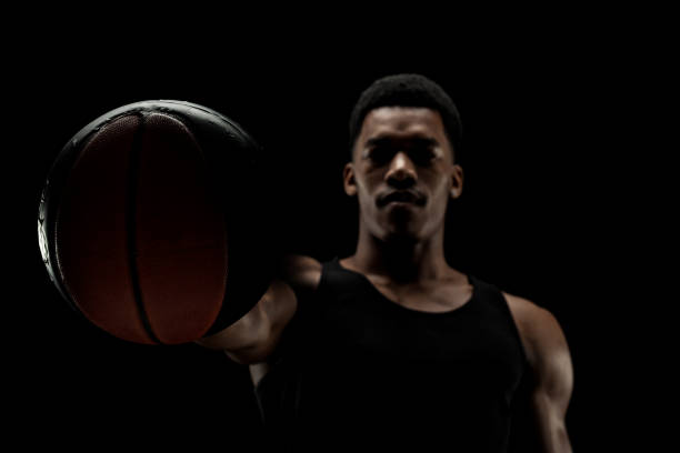 Basketball player holding a ball against black background. Serious concentrated african american man. stock photo