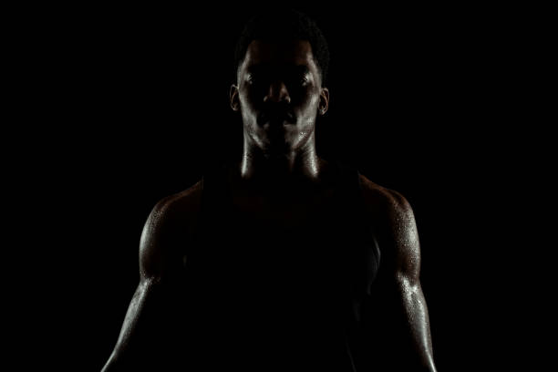 Serious concentrated african american man. Sweaty muscular person sidelit silhouette. stock photo