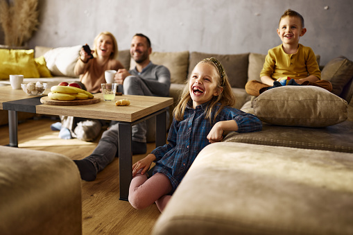 Cheerful girl having fun while watching TV with her family in the living room.