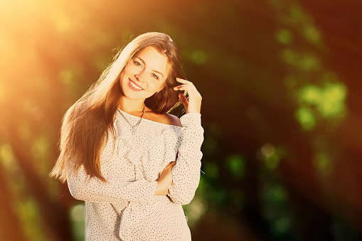 Stylish pose of a beautiful girl on which sunlight shines. The girl looks at the camera lens and smiles