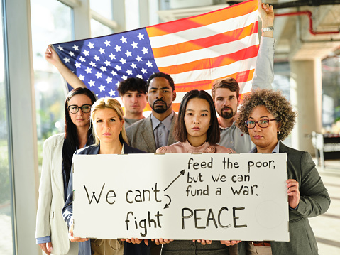 Serious entrepreneurs holding American flag and banner with a message to their government in the office and looking at camera.