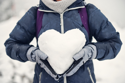 Mature woman holding a heart made of snow on a winter day.\nCold winter day. \nShot with Canon R5