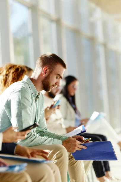 istock Young businessman using mobile phone while waiting for job interview with other candidates. 2050266744