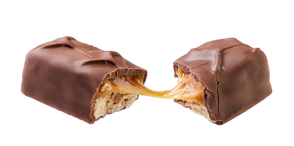 A chocolate bar with caramel and nuts broken in half flies close-up on a white background. Isolated