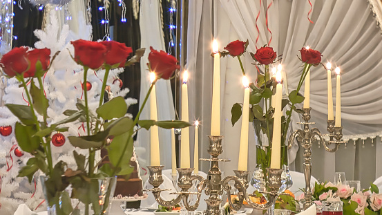 A festively decorated Christmas table. There are red roses and burning candles on the table.