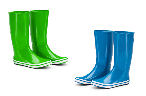 Close up color image depicting two pairs of dirty, muddy children's rubber boots outdoors in the yard. One pair is blue and the other is a vibrant lime green. Room for copy space.