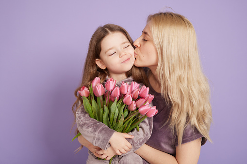 a little girl with her mother and a bouquet of flowers are hugging on a purple background, family holiday and togetherness.