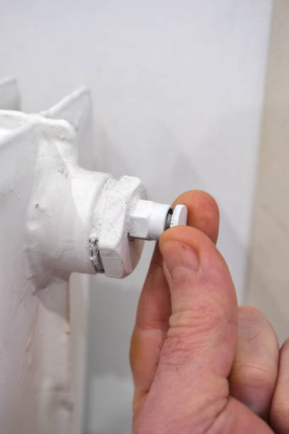 fingers turning the bleed screw on a white cast-iron radiator - drywall screw audio imagens e fotografias de stock