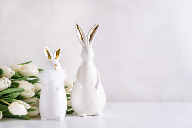 istock Two Easter rabbits figurines with bouquet of white tulips on white background. Easter celebration concept. Copy space. Front view 2050380593