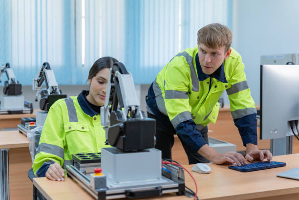 istock Two multiracial colleagues, young white man and Latin American female software engineers, wearing protective workwear working together at the small office about IT and software development for improving quality of robotic arm in their office. 2050387465