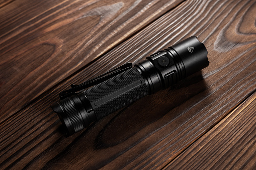 Black pocket flashlight for Everyday Carry EDC on wooden background.