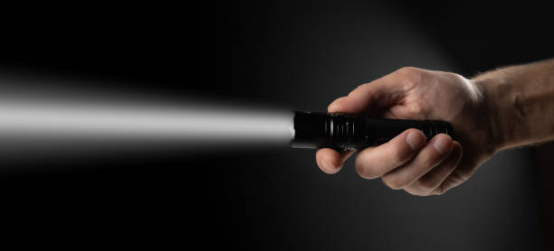 istock Black flashlight in human hands on a black background, including a white beam 2050425056