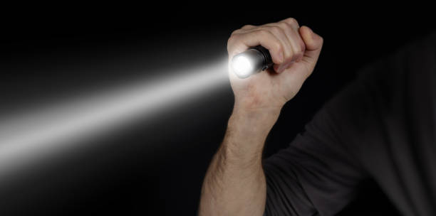 istock Male hand holding a led flashlight with a wide white beam on a black background, leaving the right side of the frame 2050425593