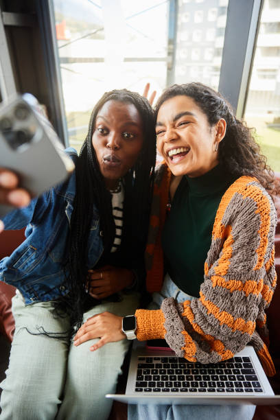 istock Smiling female college students making face and taking selfies in a student lounge 2050436844