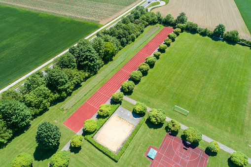 Playing fields and red, tartan running track surrounded by green areas and trees seen from above.