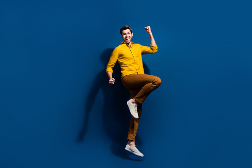 Full body photo of attractive young guy raise fists celebrate dressed stylish yellow clothes isolated on dark blue color background.