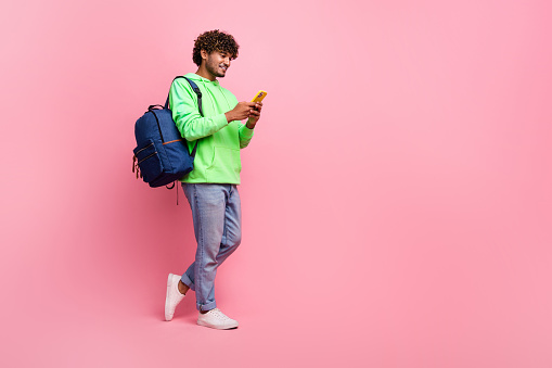 Full body photo of student arabian guy wear green sweatshirt browsing social media in smartphone isolated on pink color background.