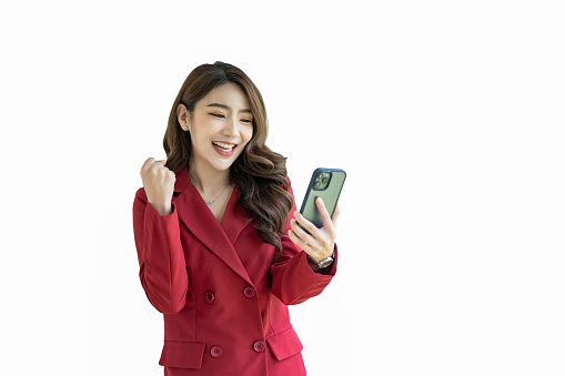 Asian businesswoman in a red suit standing with a thumbs-up gesture and holding a smartphone on a white background.