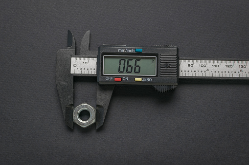 A caliper measuring a nut on a dark background. A tool for accurate measurement of dimensions.