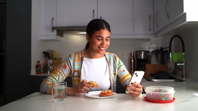 woman smiles as she checks her smartphone while enjoying a healthy breakfast