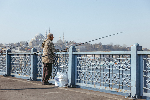 Istanbul/Turkey - 02/06/2019: Fisherman fishing on Galata Bridge in Istanbul on rainy day.
